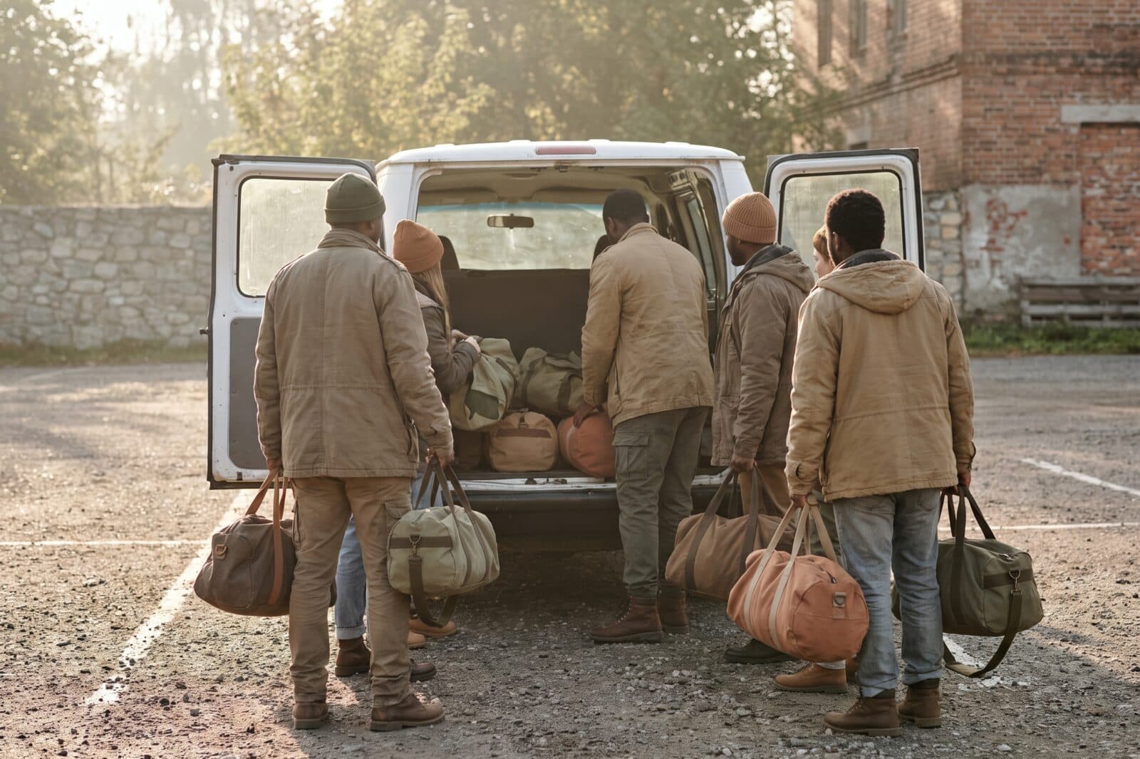 Church volunteers stacking duffel bags beside a van in a parking lot at golden hour, seen from behind.