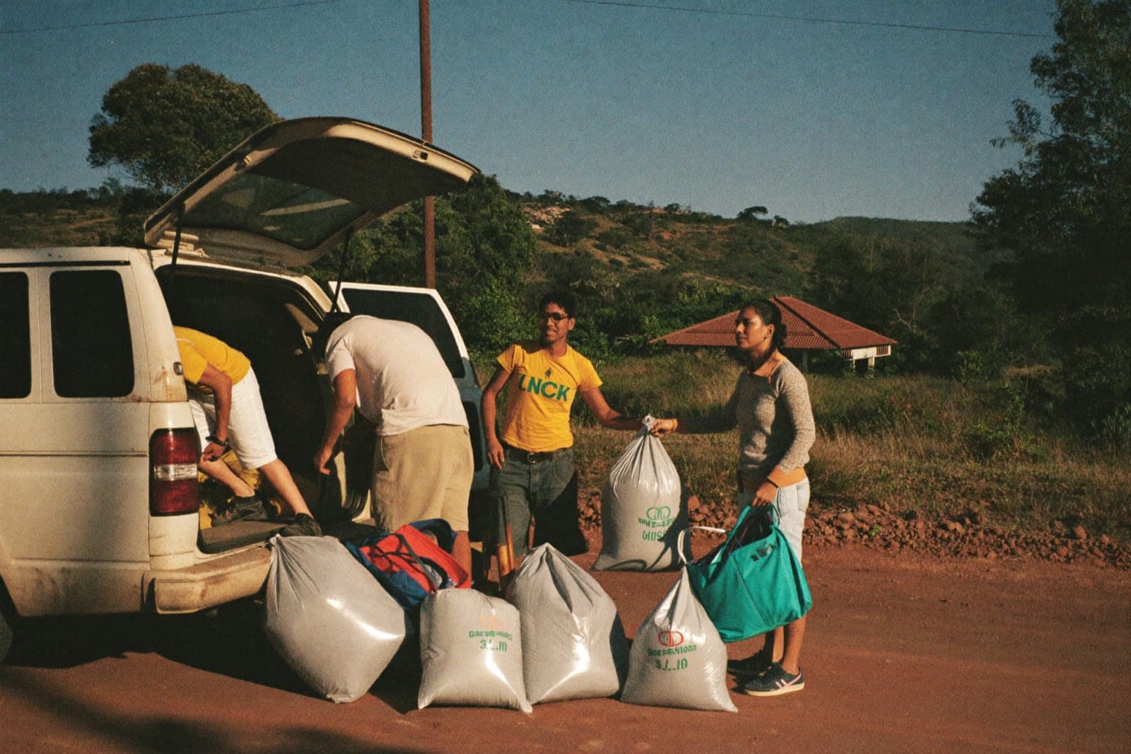 A mission team unloads duffel bags from a van on a rural road in Central America.