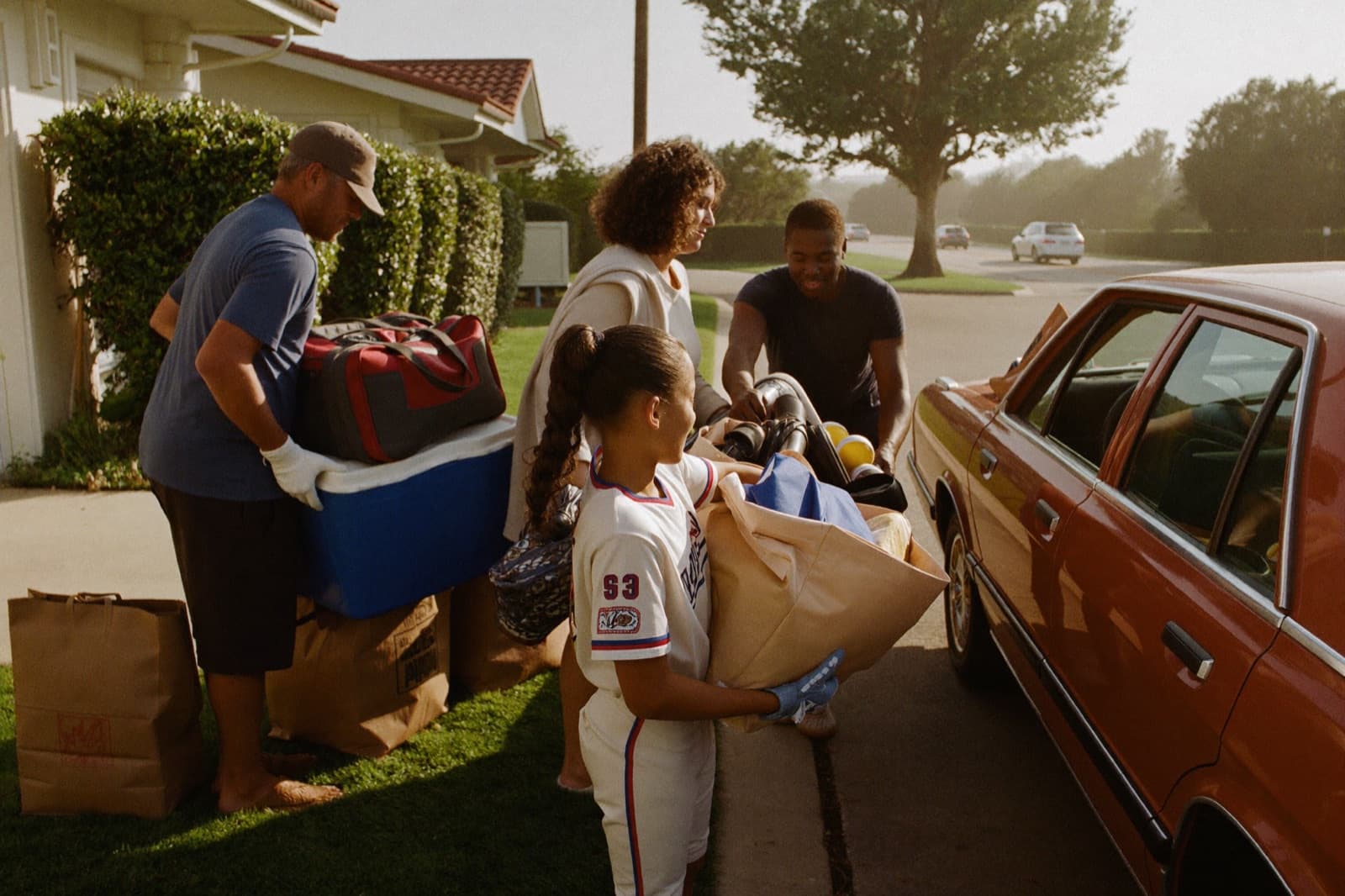 A family loads softball gear into the car in early-morning light.